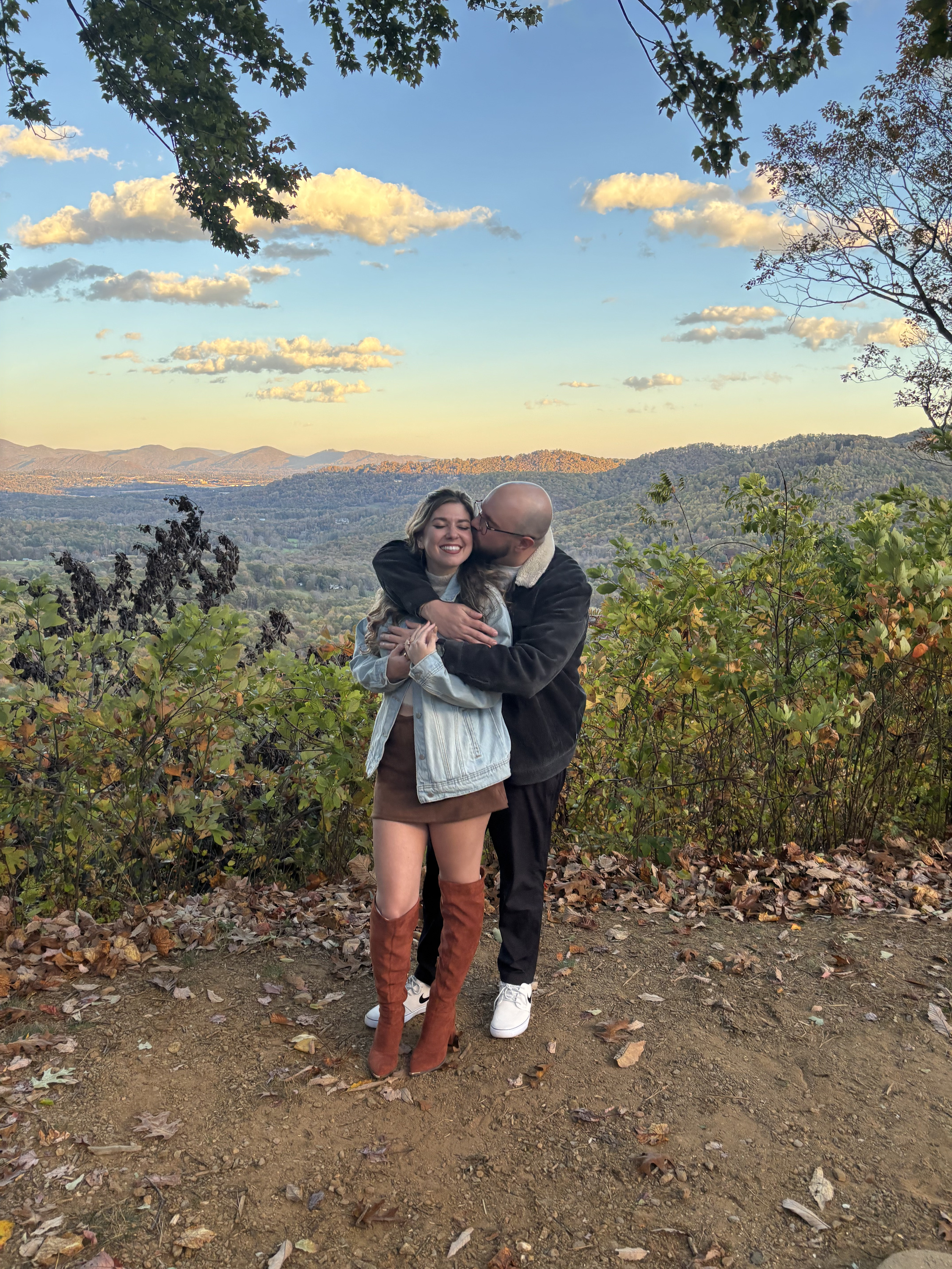 At the same overlook, one of them holding the other from behind, both laughing, autumn hills below.