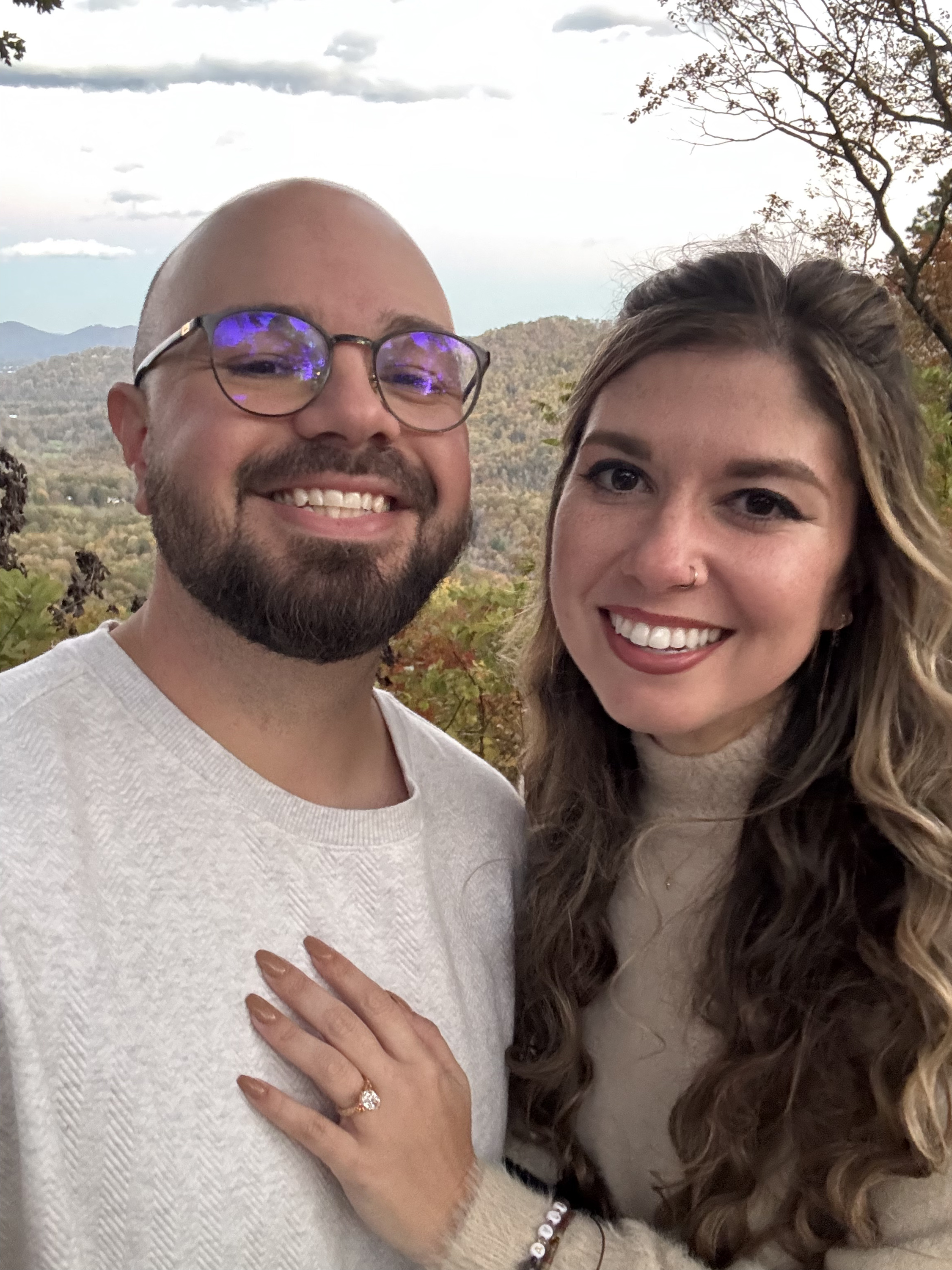 A close portrait of the two of them cheek to cheek, one hand resting on the other’s chest with an engagement ring on it.